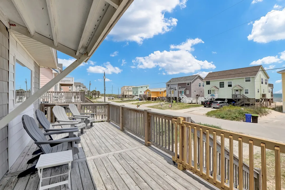 An inviting front deck with comfortable deck chairs overlooks the ocean and neighboring colorful houses. The view showcases a relaxing spot where families can unwind after a day at the beach while still enjoying the sights and sounds of the shore.
