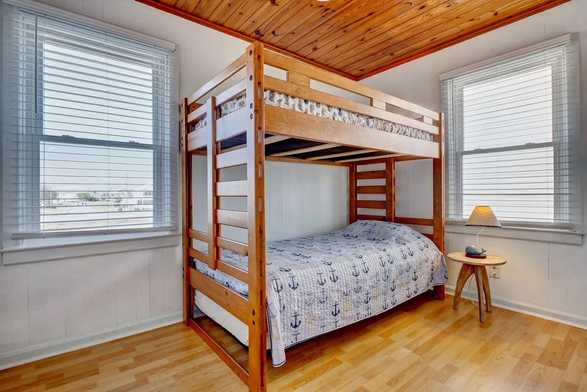 A cozy bunk room complete with a bunk bed, windows allowing in soft light, and a lamp for nighttime reading. The space feels playful and inviting, ideal for families or groups of friends.