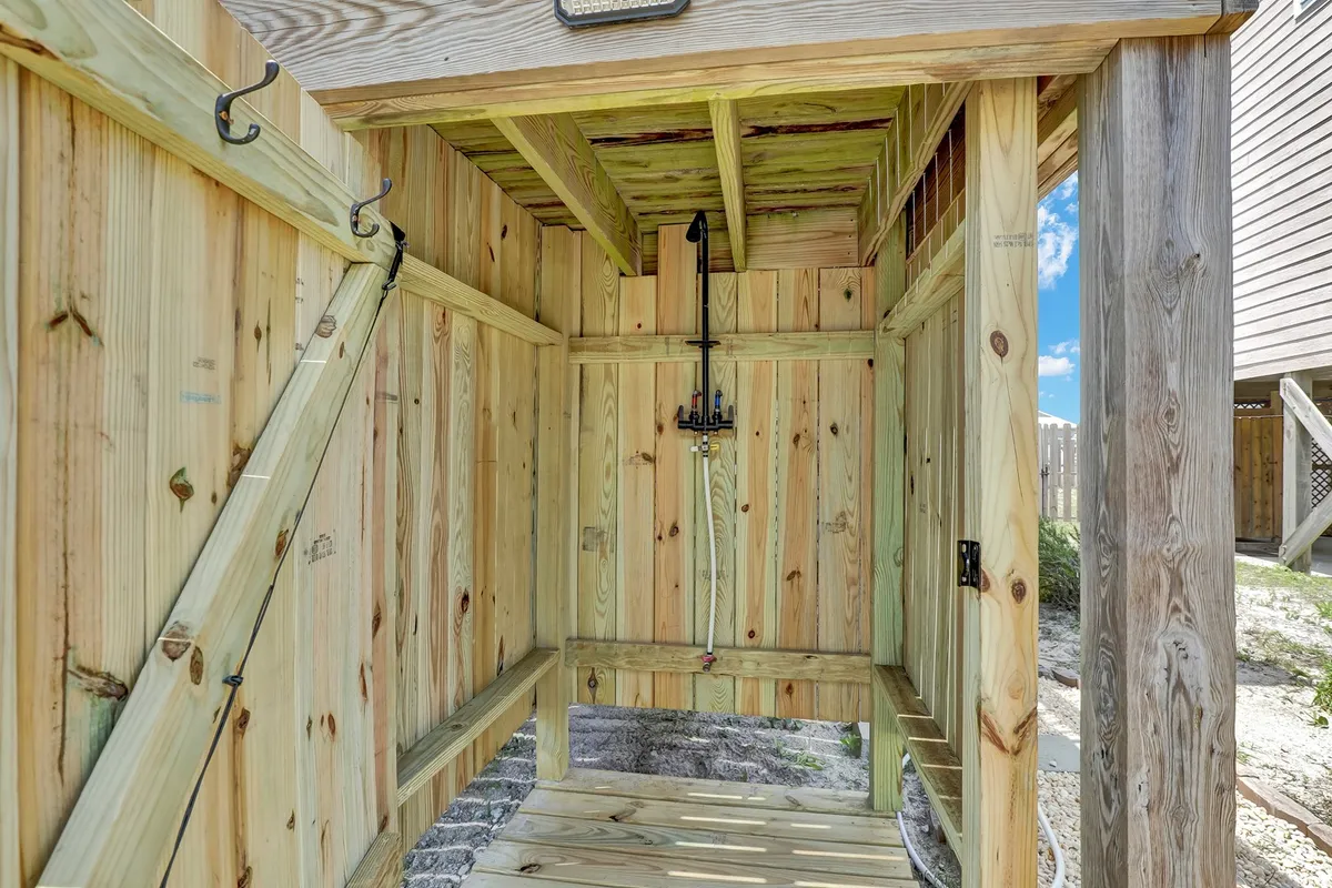 A practical, refreshing interior-to-exterior transition area featuring wooden benches, a shower fixture, and hooks for hanging beach gear—clearly designed for rinsing off after time at the beach. The space feels bright and convenient, ideal for beachgoers and pet owners.