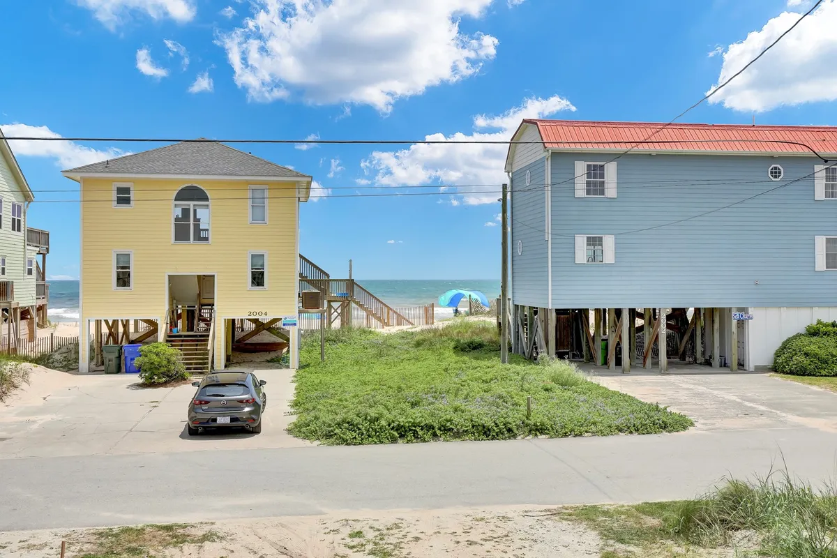 A cheerful exterior shot featuring two brightly colored houses with the ocean and sand dunes just beyond. The image captures the sunny ambiance of Surf City and suggests a close-knit, family-friendly coastal environment.